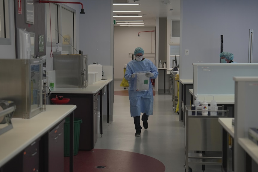 A man dressed in PPE walking through a lab with documents in his hands.