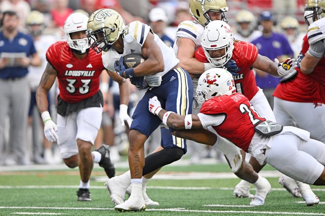 Sep 21, 2024; Louisville, Kentucky, USA; Georgia Tech Yellow Jackets running back Trelain Maddox (28) tries to break free from the tackle of Louisville Cardinals defensive back M.J. Griffin (26) during the second half at L&N Federal Credit Union Stadium. Mandatory Credit: Jamie Rhodes-Imagn Images