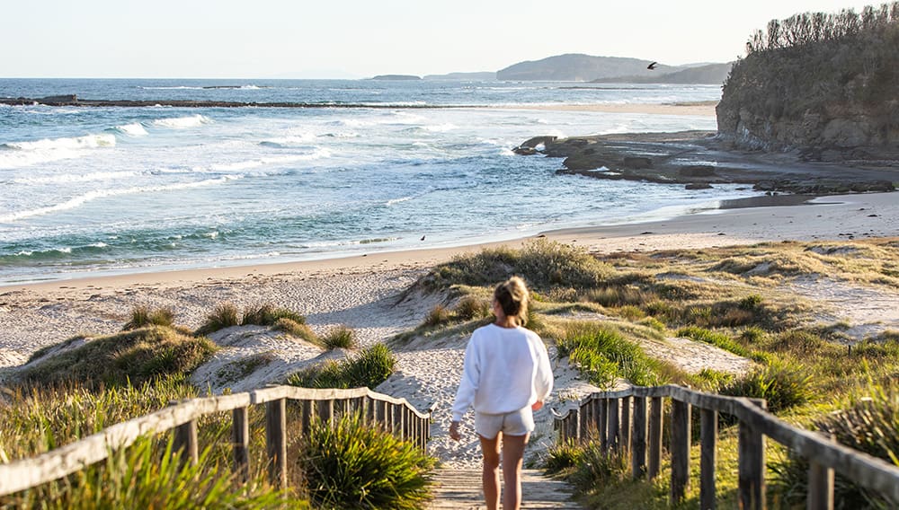 Woman walking down onto Pretty Beach, Murramarang National Park. Image: Shoalhaven City Council/Josh Burkinshaw