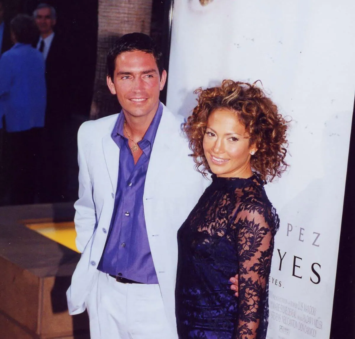 Jim Caviezel and Jennifer Lopez stand together on the red carpet. He wears a white suit and she wears a black dress.