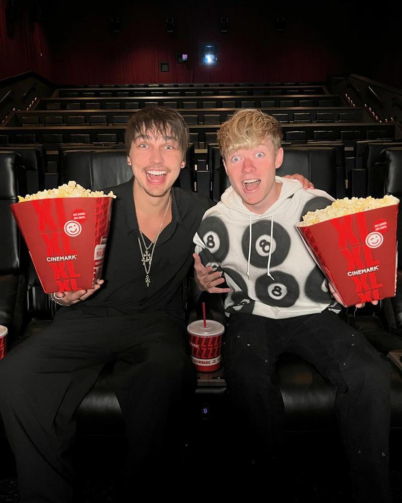 Sam and Colby sitting in a movie theater holding bags of popcorn