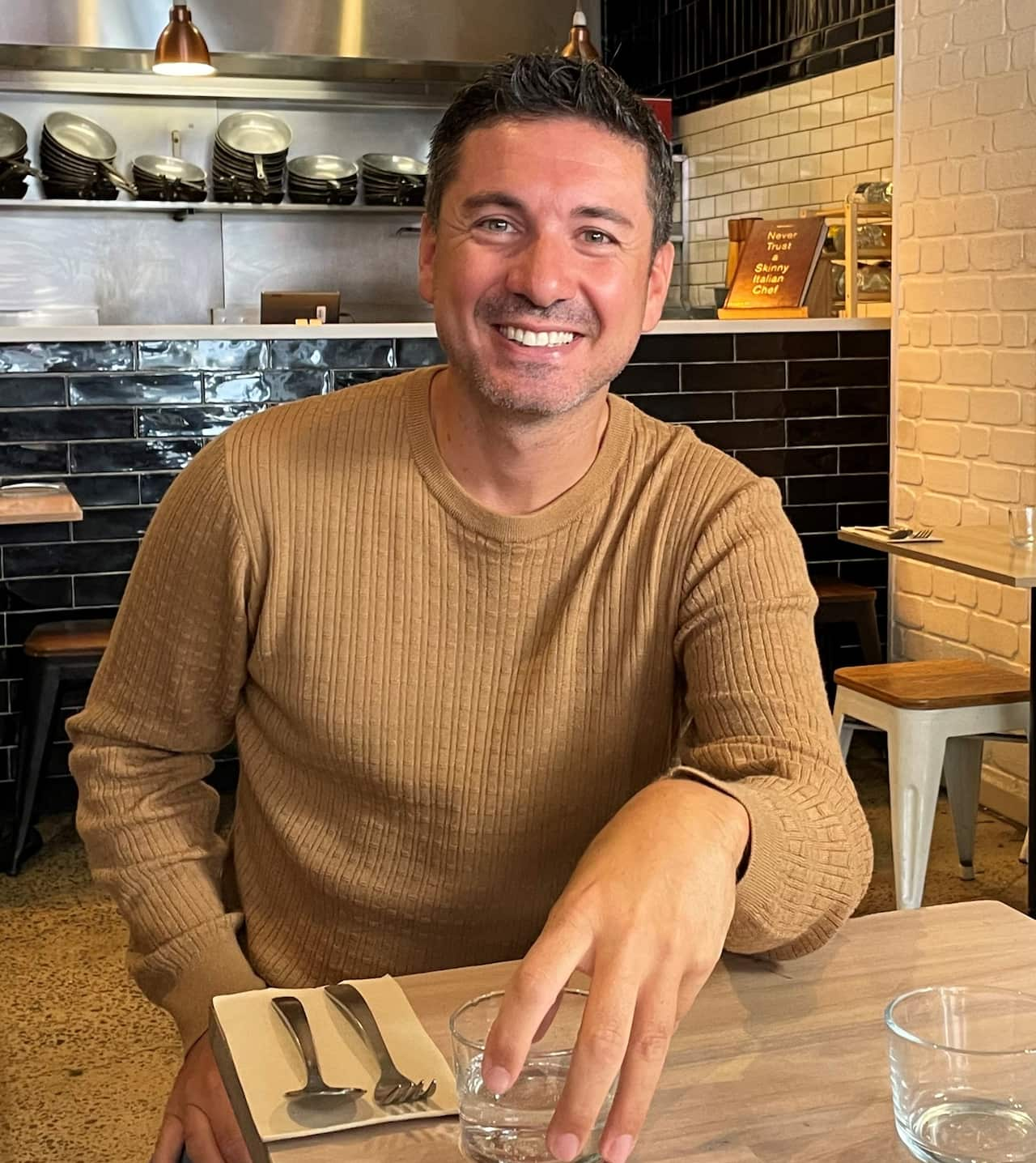 A man in an orange jumper sits at a table inside a restaurant. 