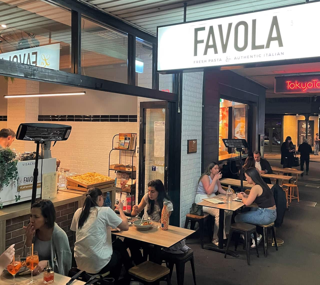 The outside of a small restaurant with patrons sitting at tables.