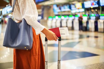 close up of unrecognizable female passenger at check-in counter in airport terminal, with luggage and passport