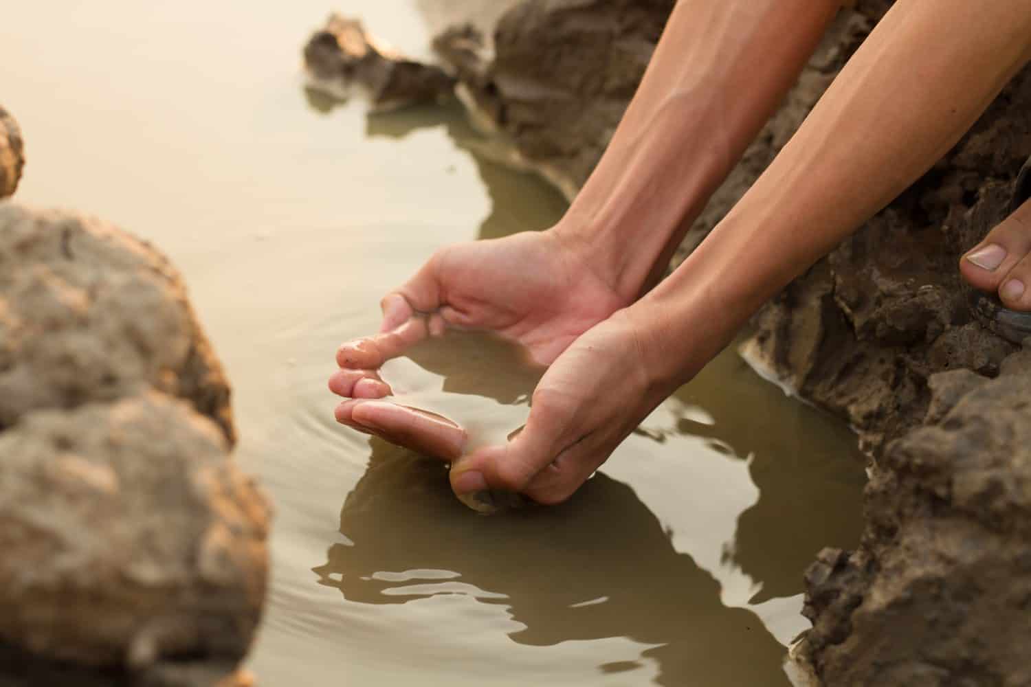 Hand taking water from dirty pond metaphor freshwater scarcity, drinking water and environment issue concept