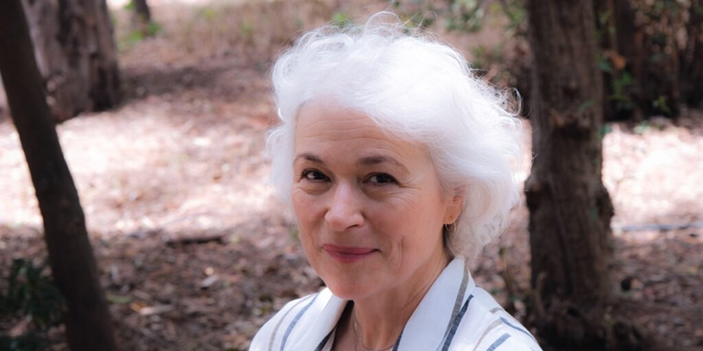 Vangelio Andreadaki_image by Dorothea Voyatzi. Image of a smiling woman with short white hair wearing a white blouse with dark stripes.