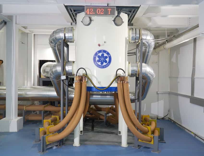 A photograph of a large contraption. It is a white cylinder with multiple hoses coming out of it