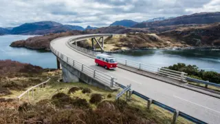 Getty Images A red and white campervan crosses the Kylesku Bridge. The bridge is set in a Highland landscape of hills and lochs.