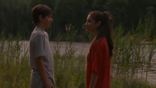 Two kids looking at each other in front of a lake