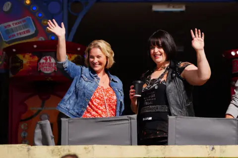 PA Media Joanne Page and Ruth Jones wave at cameras from outside an arcade on Barry Island, Wales