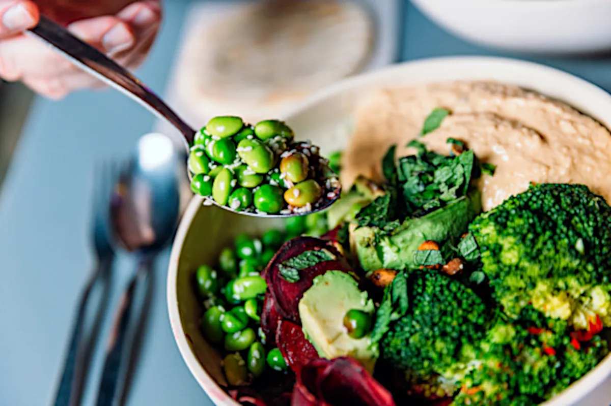 Closeup of a plate of vegetables and someone grabbing a spoonful of them.