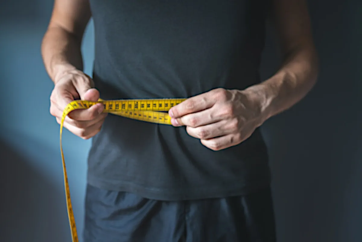 A person measuring their waist with a measuring tape.