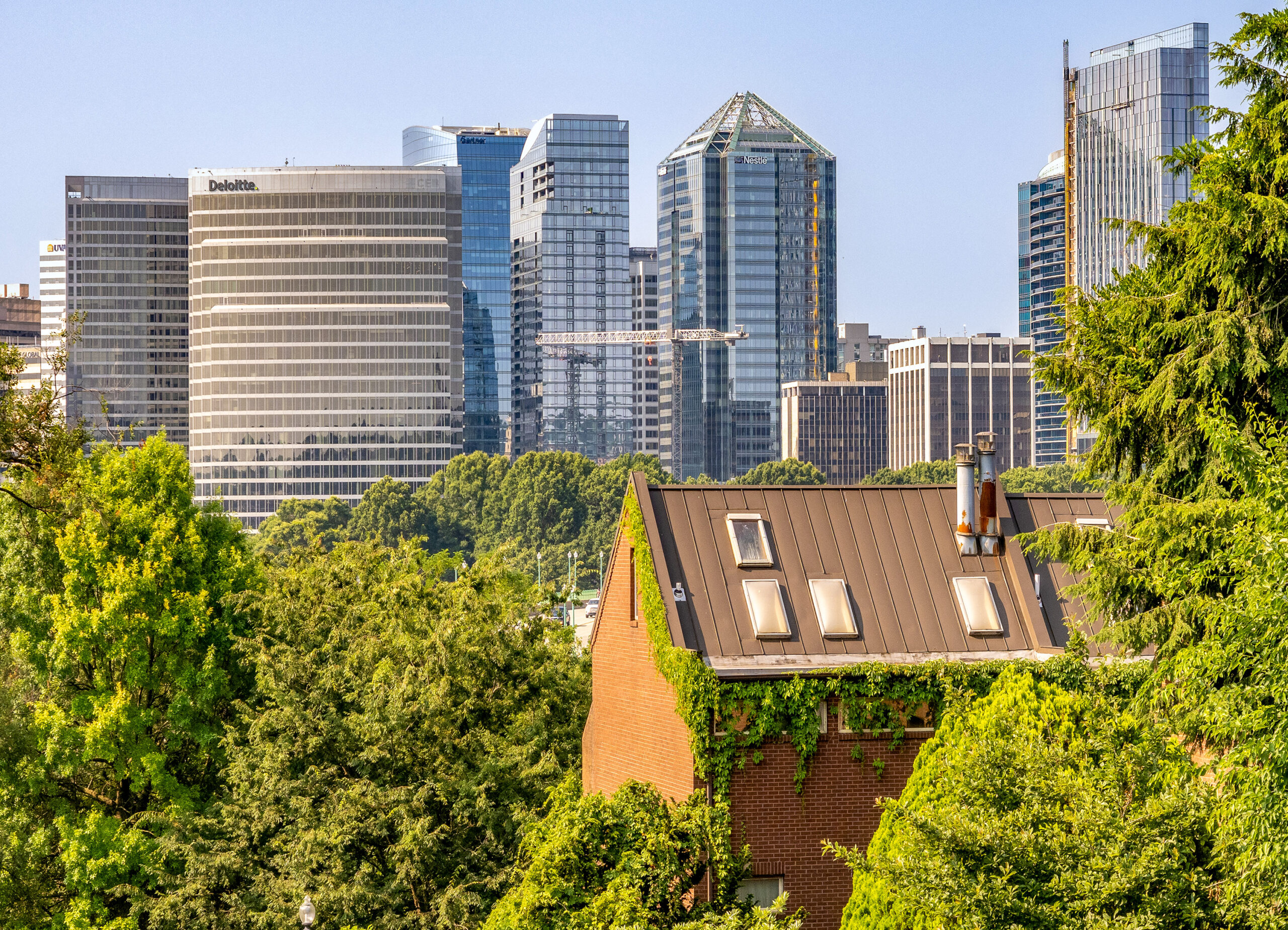 Elevated view of a residential house with ivy-covered walls and a modern city skyline with high-rise buildings in the background on a clear day.