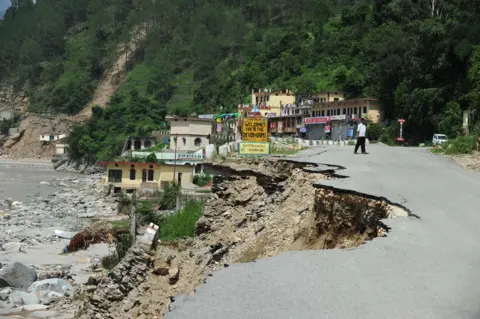 Getty Images A road beside a river has been washed away by flood water in India.  A small town can be seen in the background.