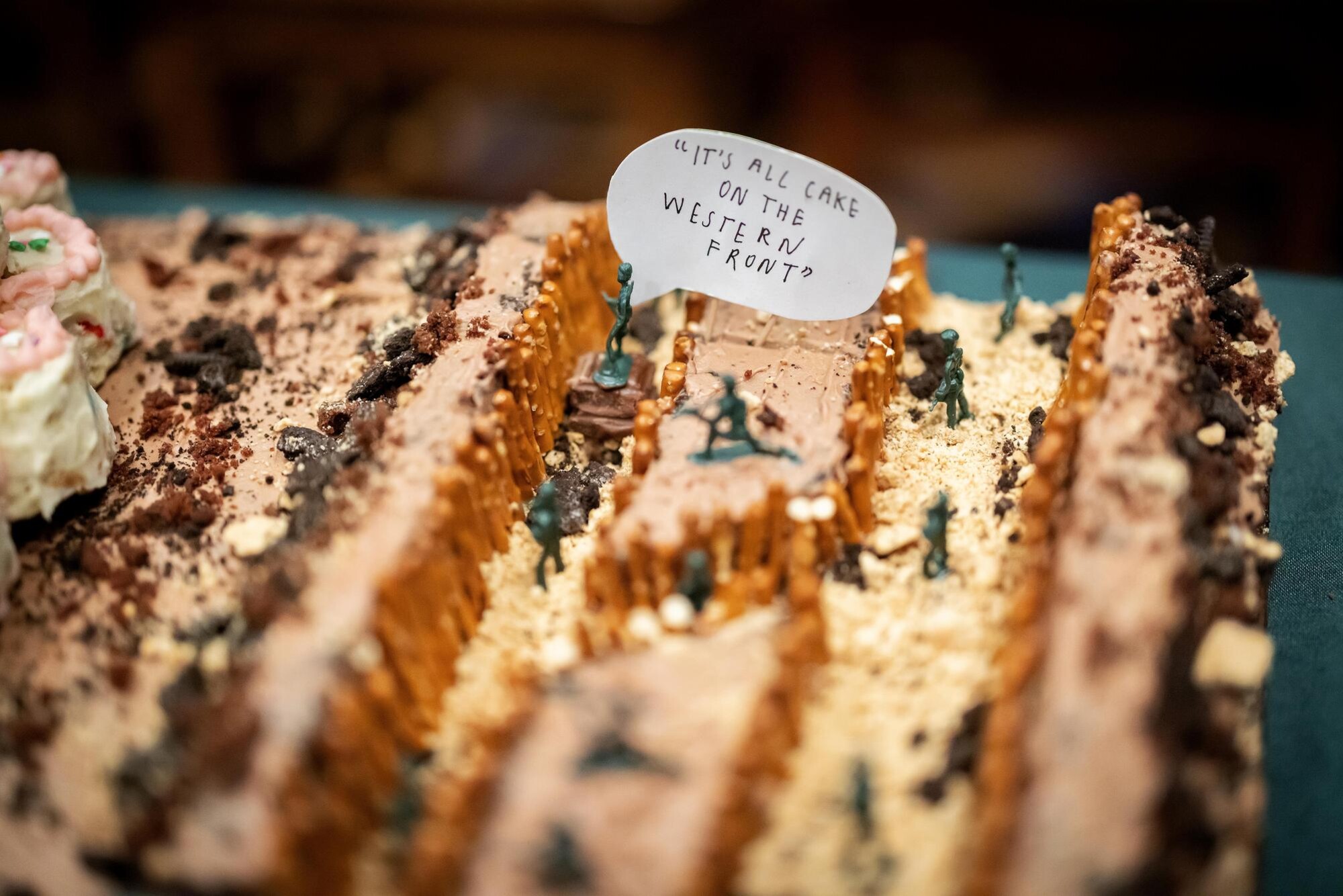 A closeup view of a cake decorated with toy soldiers and a sign reading “It’s all cake on the western front.”