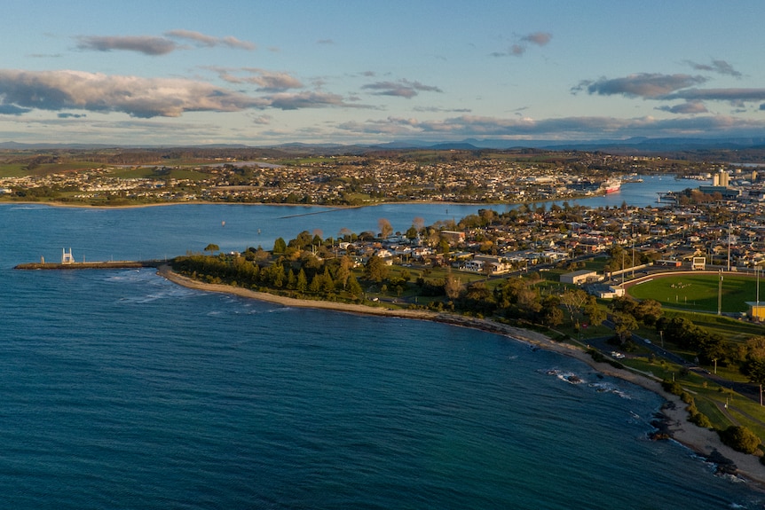 Aerial view of a distance red ship moored on a river at sunset with houses and coastline in the foreground.