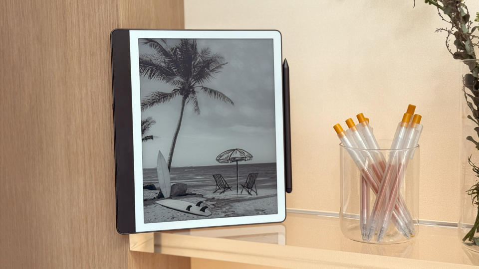 The Amazon Kindle Scribe on a shelf with its screen facing out and the companion pen attached magnetically to its right side.