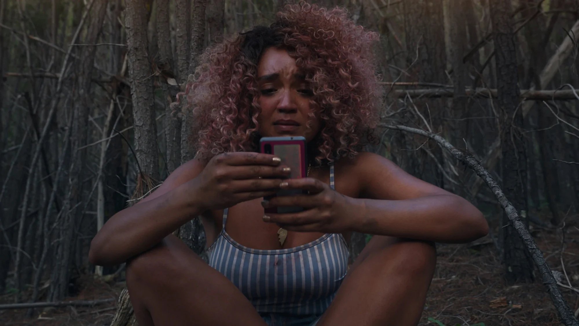 Aisha Dee sits in distress looking at her phone in the film 