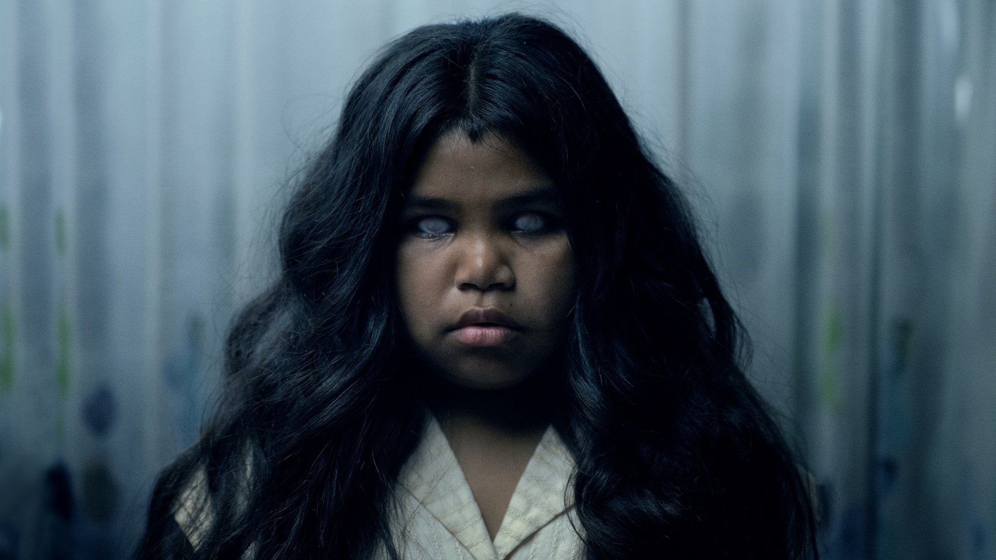 A young girl with white eyes stares at the camera in a still for 