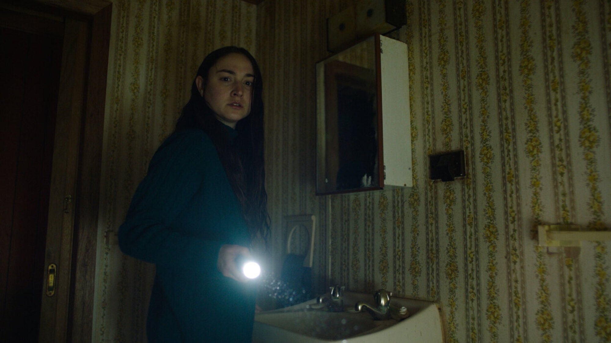 Jordan Cowan shines a torch into a dark bathroom in the film 