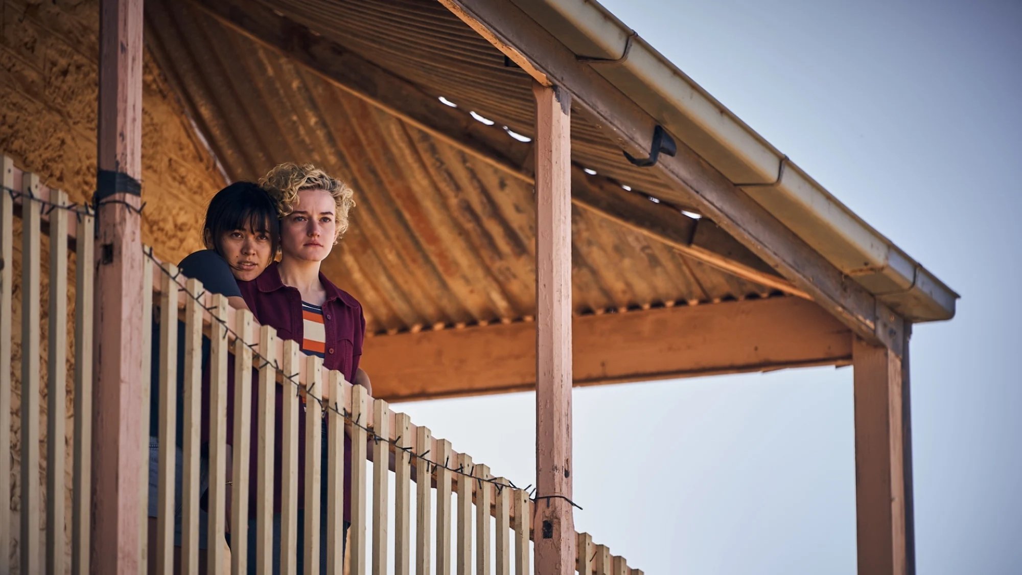 Jessica Henwick and Julia Garner stand on a pub verandah looking worried in the film 