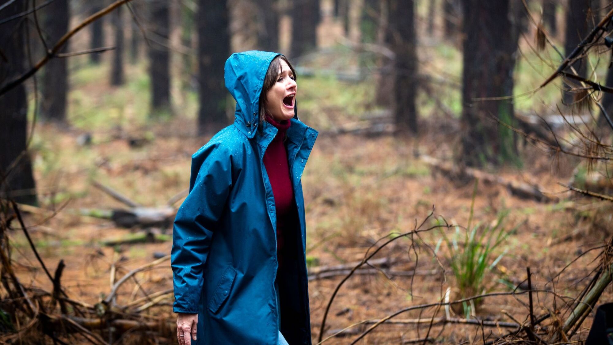 Emily Mortimer stands in a forest wearing a blue jacket screaming in the film 