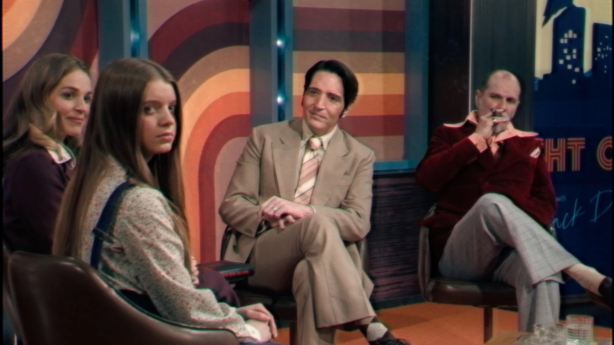 A late night show host interviews three people on a '70s set in the film 