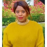 Photo of Pamela Sweeney. Pamela is wearing a yellow jumper and is standing in a garden.