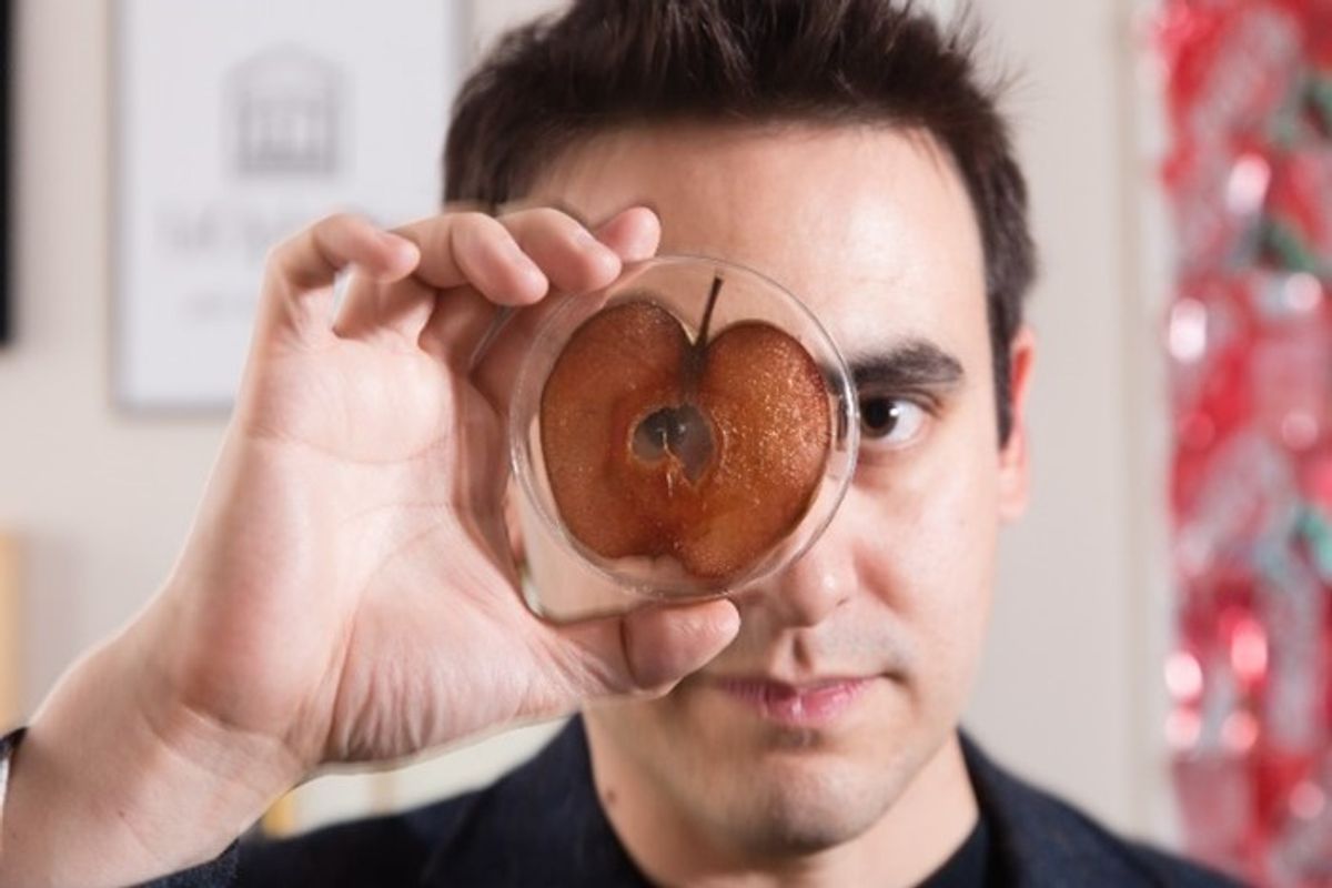 A photo of Andrew Pelling holding a Petri dish with a browning apple inside of it close to his face.