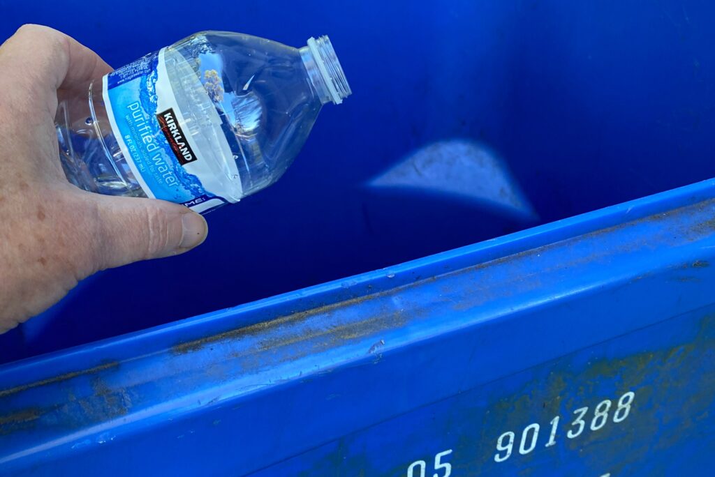 A woman's hand places a plastic water bottle into a recycling bin