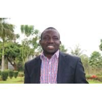 Headshot of Segun Fatumo. Segan is wearing a checked shirt and a black jacket. He is standing outside, surrounded by trees.