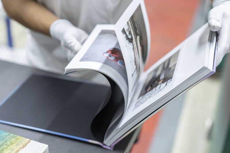 A person wearing white gloves flips through the pages of a photo book on a table. The pages contain photographs. The background is slightly blurred, focusing on the book.