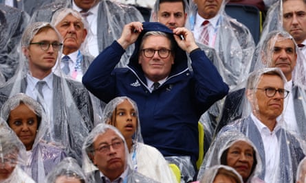 Keir Starmer pulls up his hood while standing among other people wearing rain macs