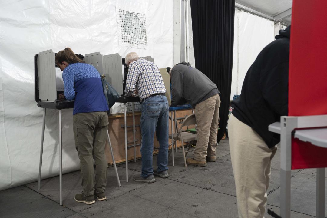 Four people stand at voting stations.