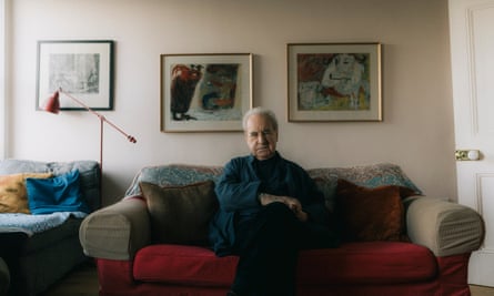 John Banville sits with his arms folded in the middle of a sofa in a living room