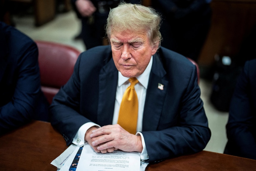 Trump looks down frowning while wearing a suit in court