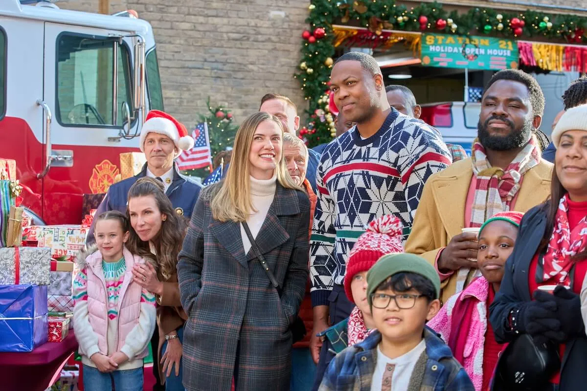 A man and a woman standing among a group of kids in front of a fire truck