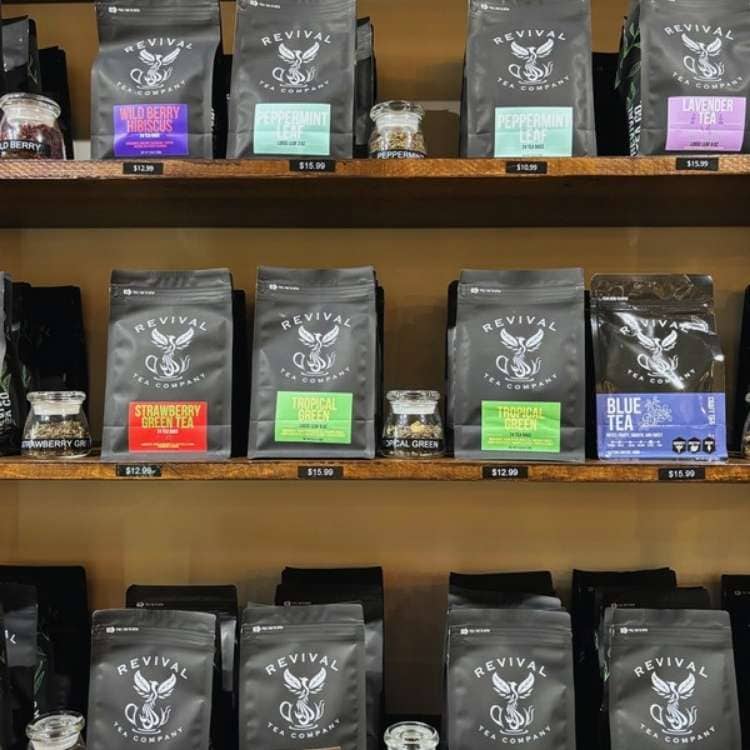 Black bags of looseleaf teas on shelves with colorful labels in green, purple, and red.