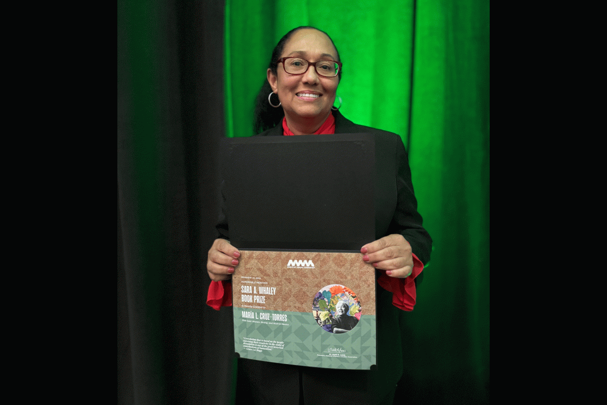 ASU Associate Professor Maria Cruz-Torres holds a folder with a certificate for her honorable mention