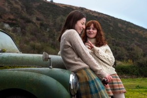 SAY NOTHING is a Hulu series produced by FX about The Troubles. Shown here are Hazel Doupe as Marian Price and Lola Petticrew as Dolours Price, leaning against a green car parked in front of a hill