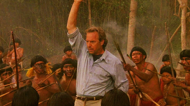 Dr. Joe Darrow stands with his arm in the air surrounded by a tribe holding spears