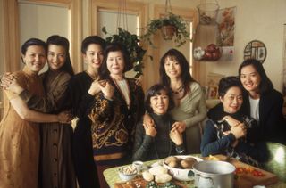 the cast of the joy luck club smiles while surrounding a table of food