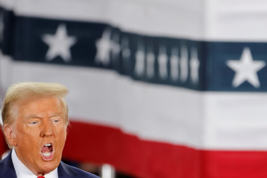 Donald Trump with his mouth open in front of a red, white and blue background