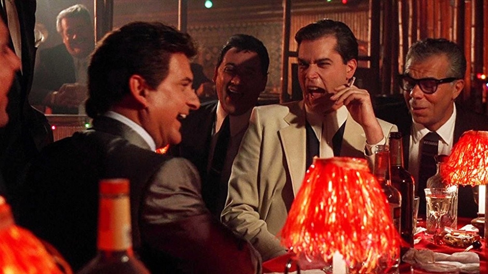 Joe Pesci and Ray Liotta laughing at a table surrounded by men in suits in Goodfellas.