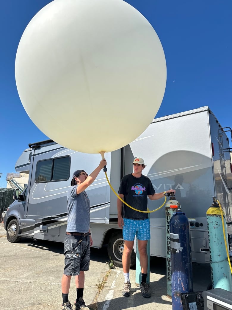 One man holds on to a large balloon while another watches. 