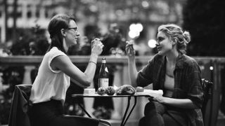 two women eat pastries at a cafe table outside in frances ha