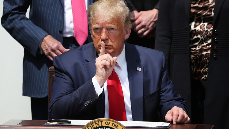 Donald Trump with finger to lips at desk before bill