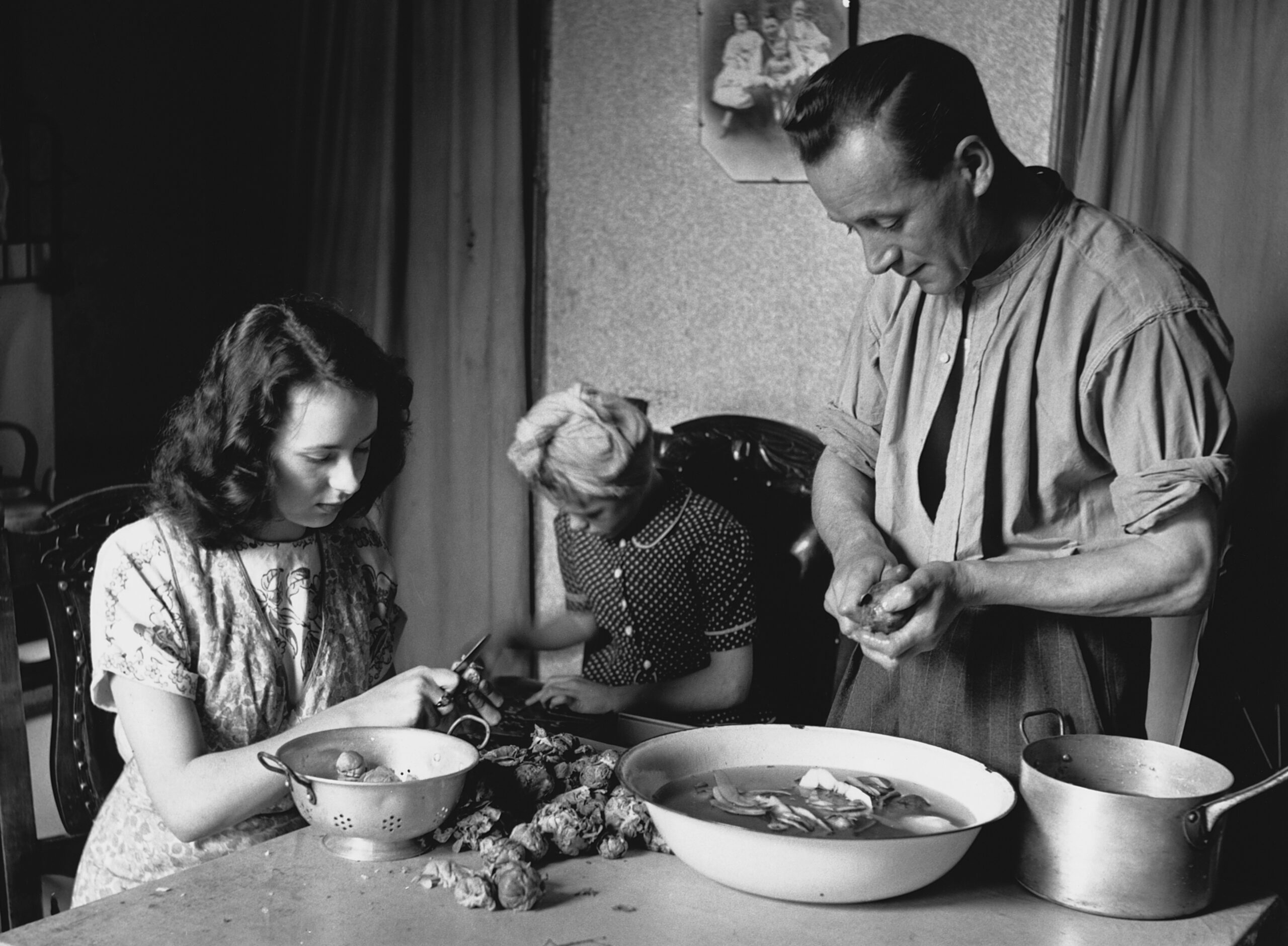 A woman and man prepare vegetables, while a child looks on.