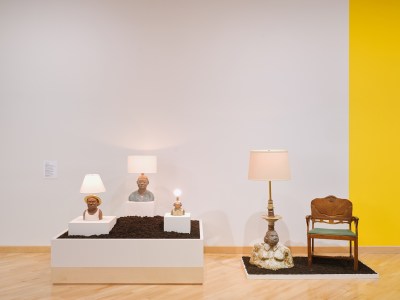 Museum installation view showing sculptures of human busts with lamps coming out of their heads. 