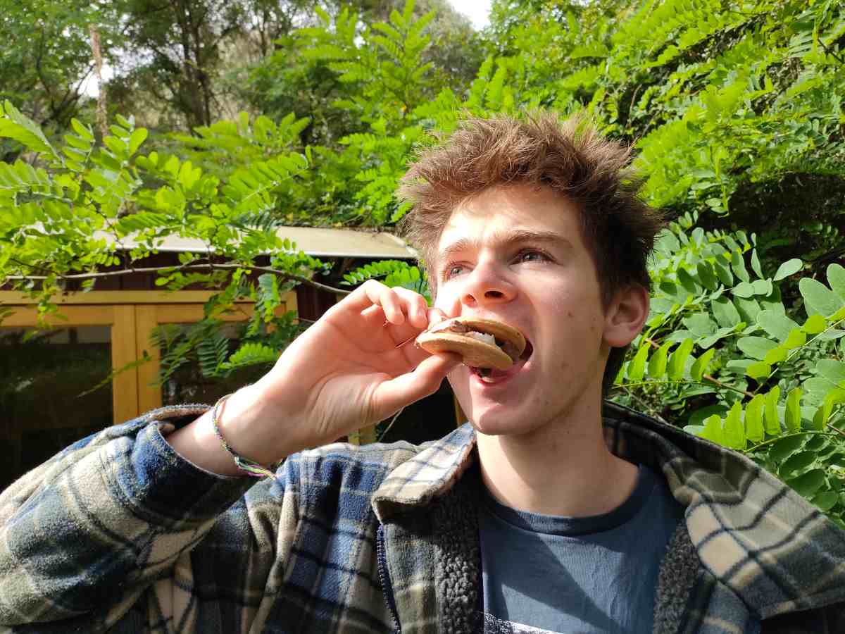 A teenage boy eating a s'more from a solar oven, one of the hands-on activities